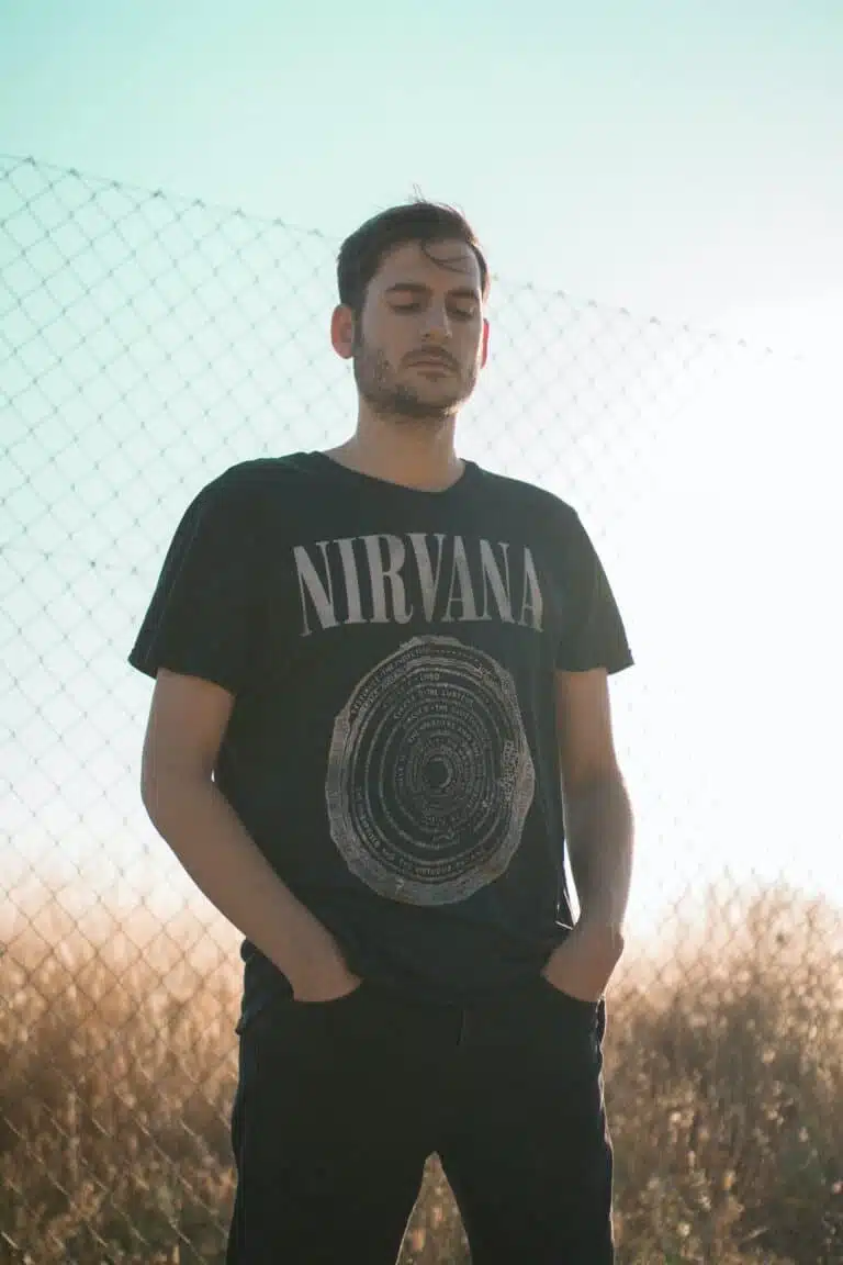 Man posing in front of a fence wearing a Nirvana t-shirt. Selling merch can make you money online 