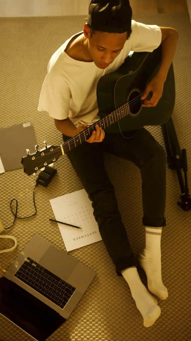 Overheat shot of someone practicing guitar next to a laptop
